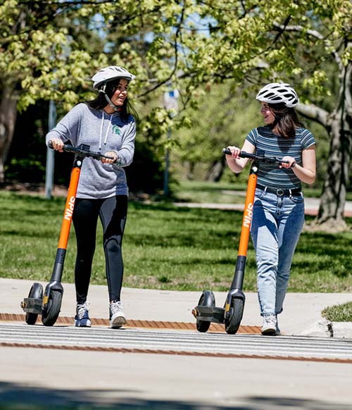 Two people walk with Spin scooters.