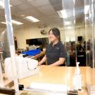 Smiling student employee behind plexiglass at Student Accounting service desk with computer